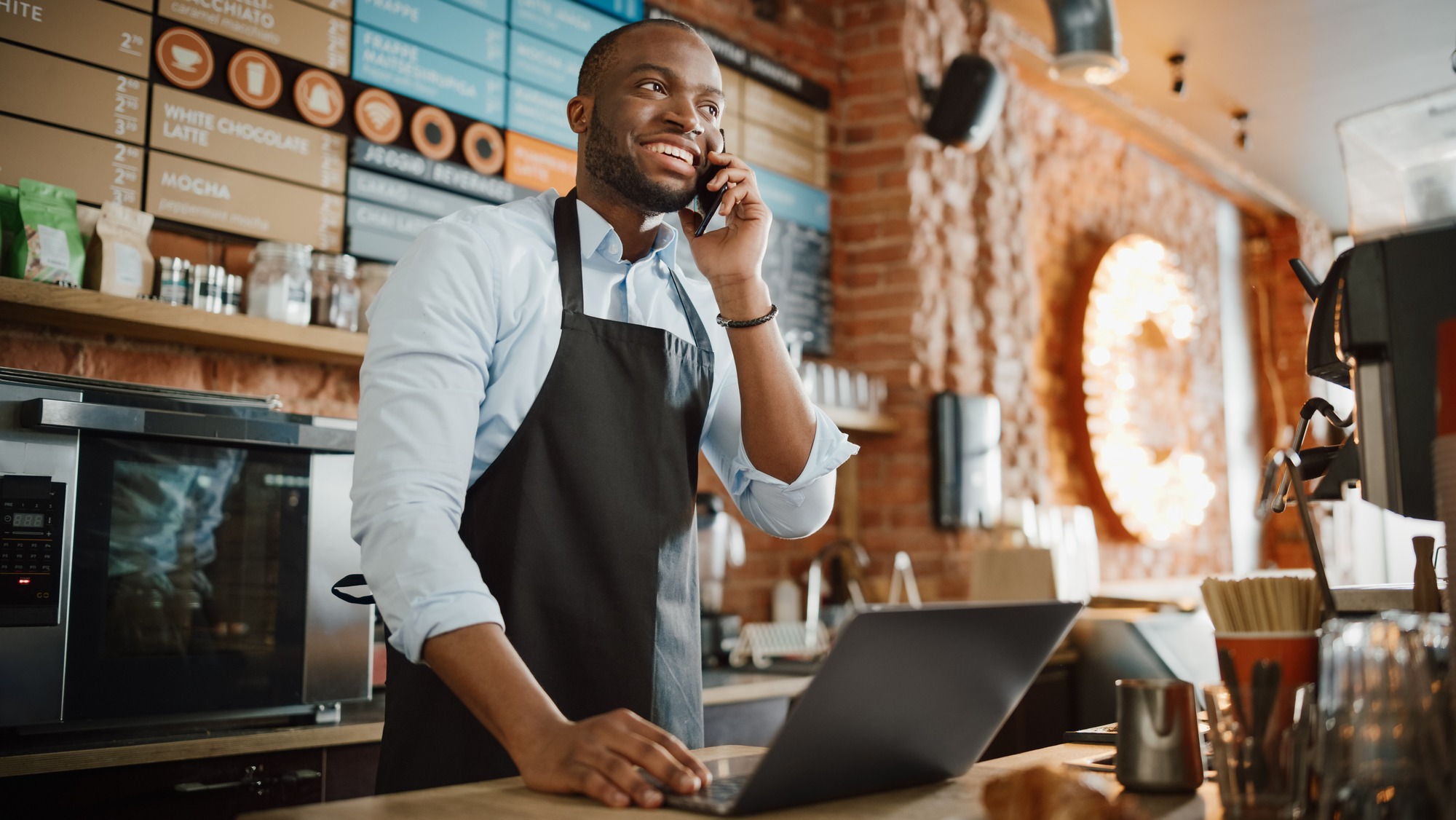 Black African American Coffee Shop Employee Accepts a Pre-Order on a Mobile Phone Call